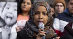 representative ilhan omar speaking into a microphone with a blurry crowd behind her