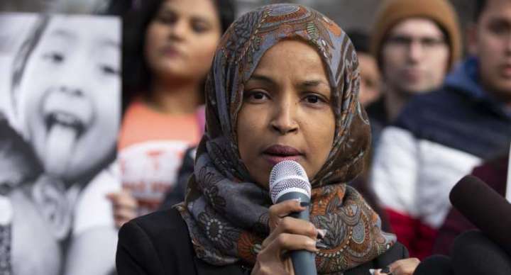 representative ilhan omar speaking into a microphone with a blurry crowd behind her